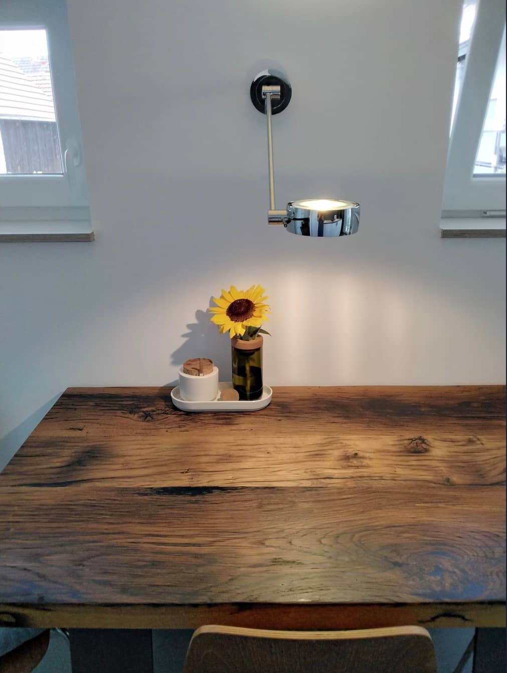 Esstisch aus Altholz mit Wandleuchte und einer Sonnenblume